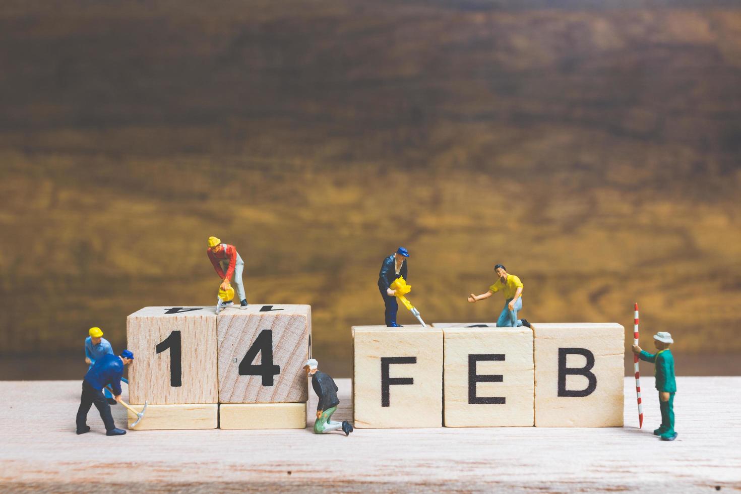 Trabajadores en miniatura construyendo las palabras y fechas para el día de San Valentín en bloques de madera con fondo de madera, concepto del día de San Valentín foto