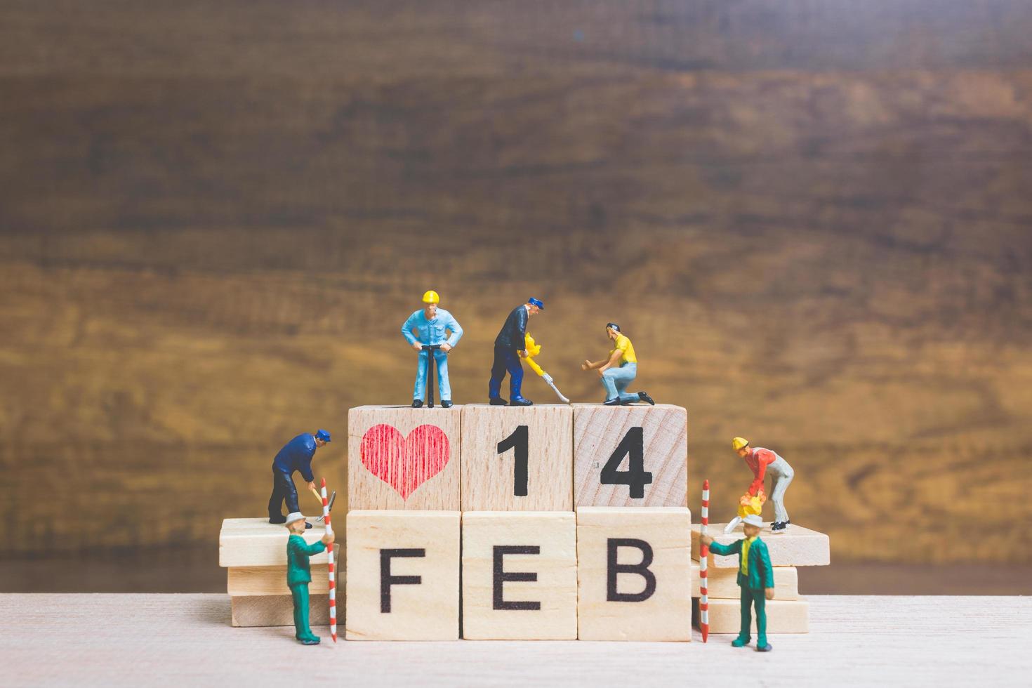Miniature workers building the words and dates for Valentine's Day on wooden blocks with wooden background, Valentine's Day concept photo