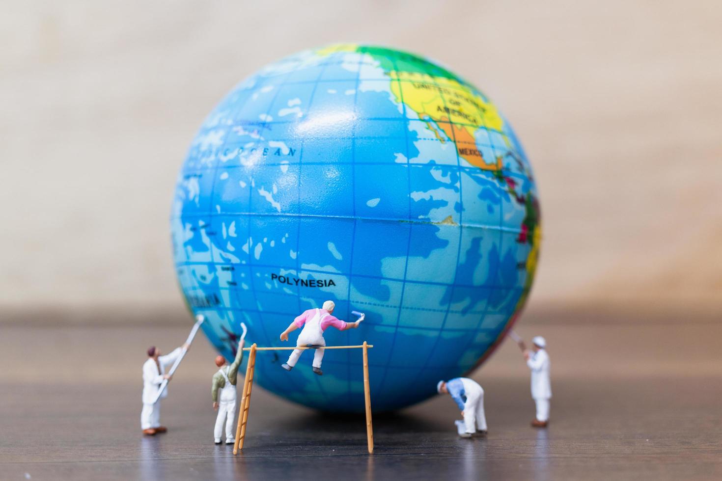 Miniature painters painting on a globe with a wooden background, save the Earth concept photo