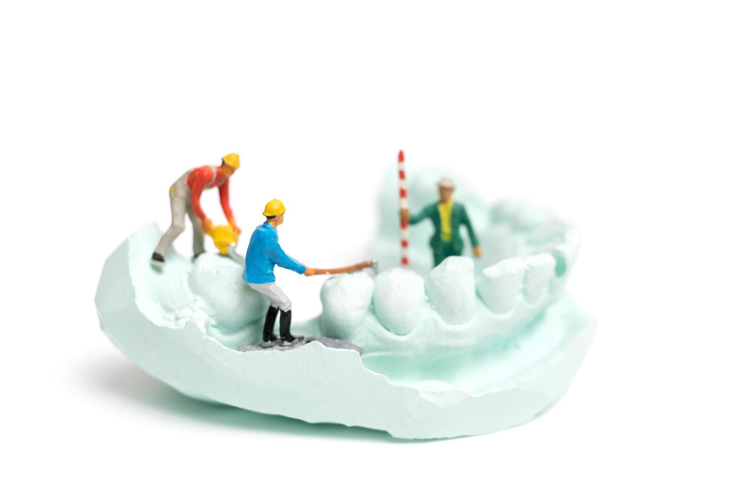 Trabajadores en miniatura llenando dientes falsos y colocándolos en una dentadura postiza hecha con yeso, concepto de laboratorio de prótesis dentales foto