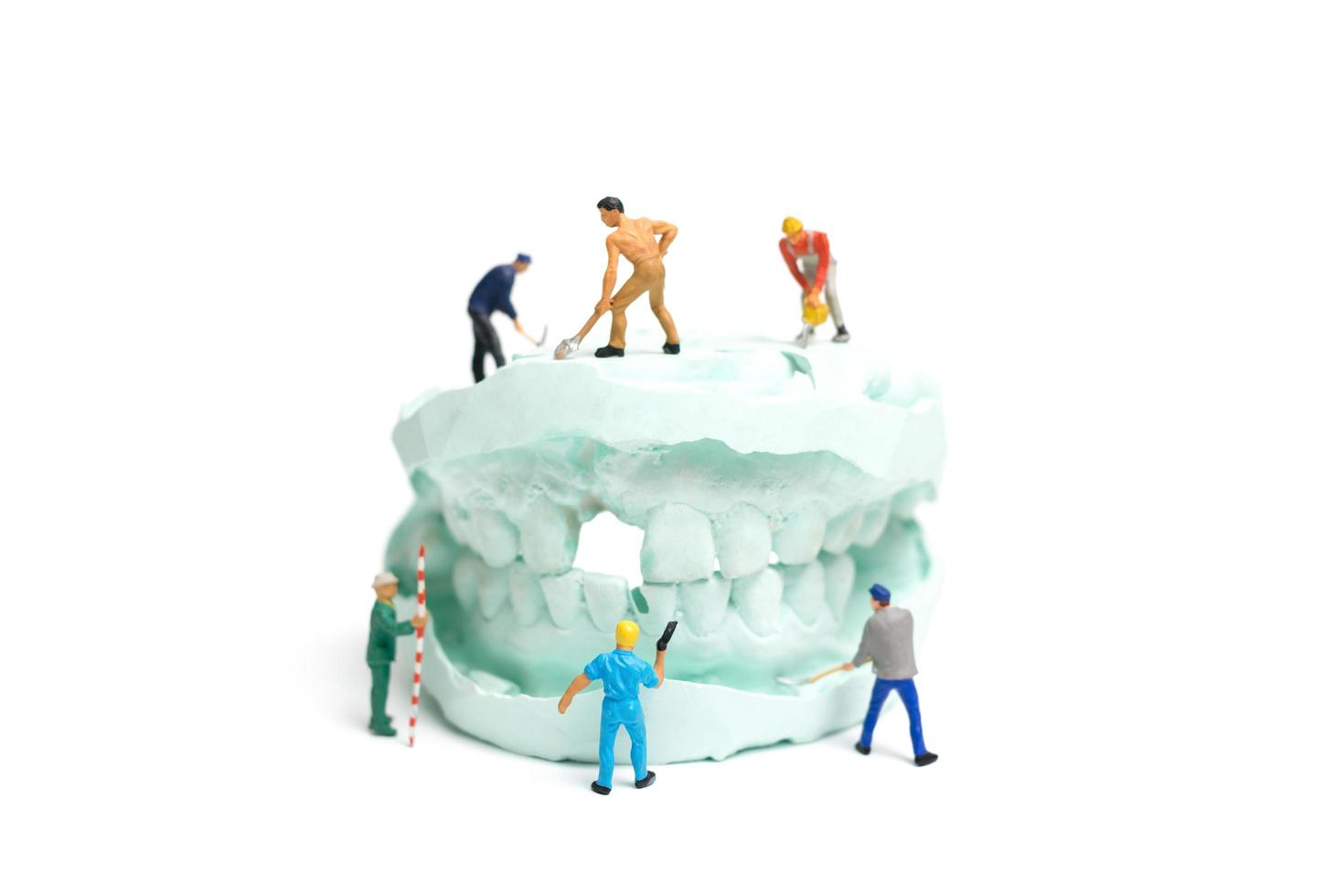 Miniature workers filling fake teeth and placing them in a denture made with plaster, dental prosthesis laboratory concept photo