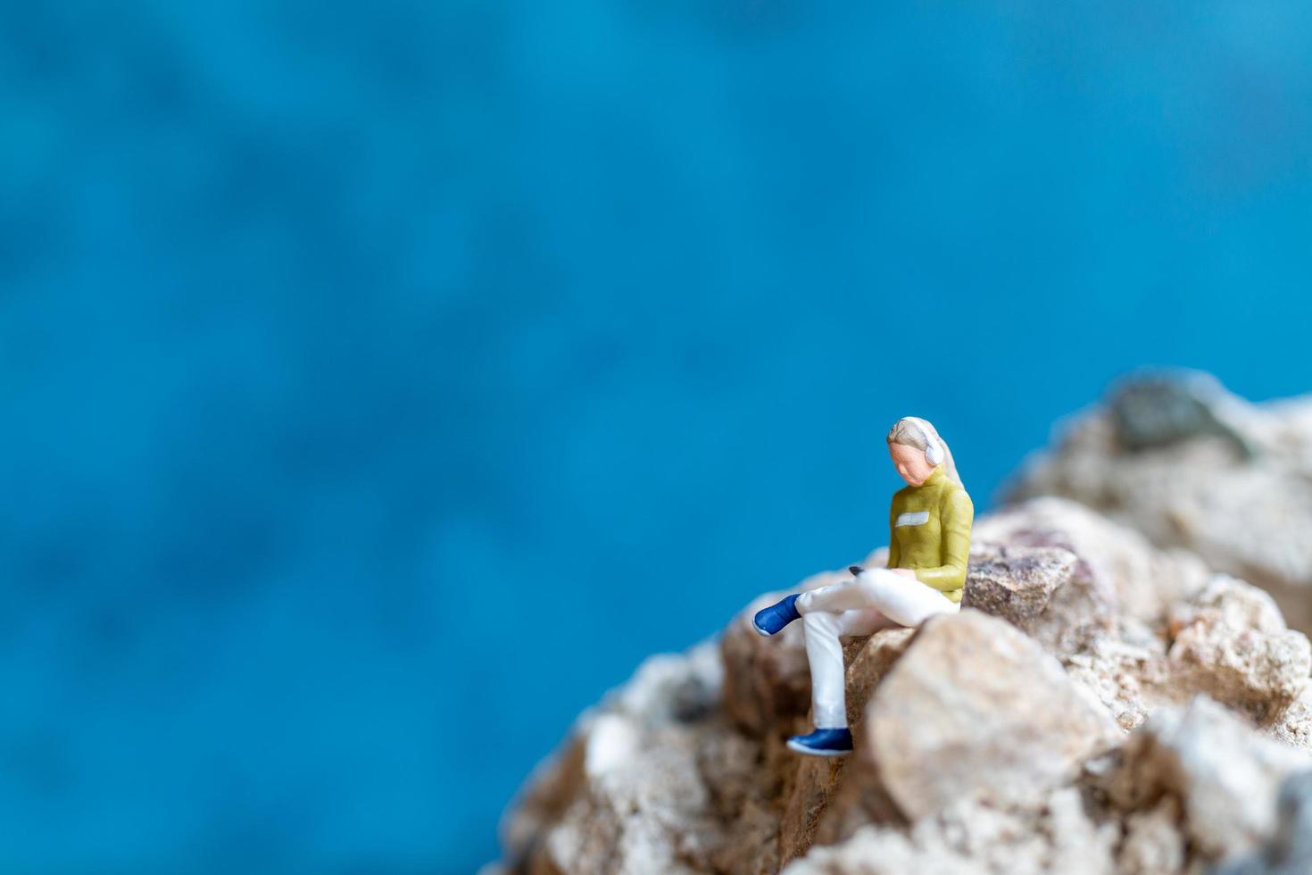 Miniature woman wearing headphones and listening to music on a smartphone sitting on the rock photo