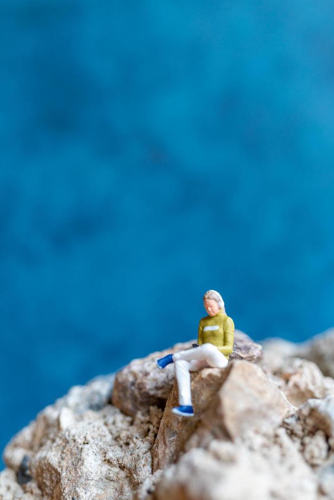 Mujer en miniatura usando audífonos y escuchando música en un teléfono inteligente sentado en la roca foto