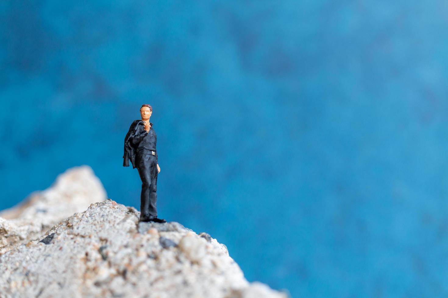 Miniature businessman standing on a rock with a blue background photo
