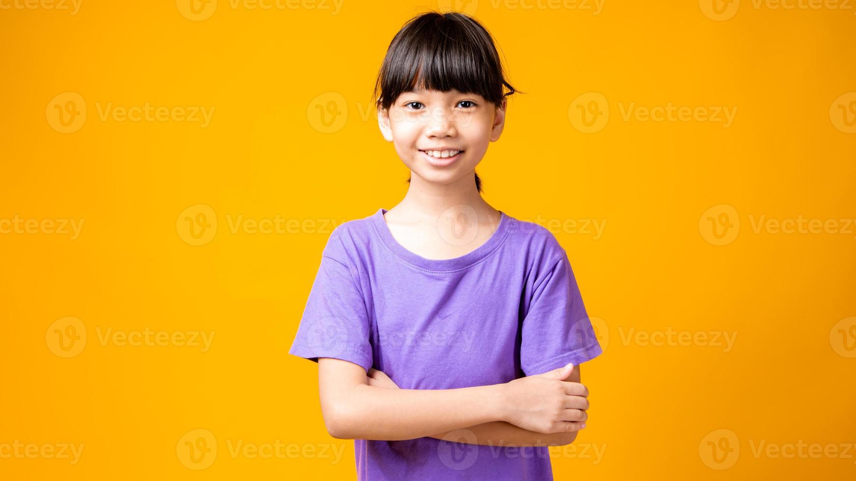 Joven asiática en camisa púrpura sonriendo con los brazos cruzados en estudio con fondo amarillo foto