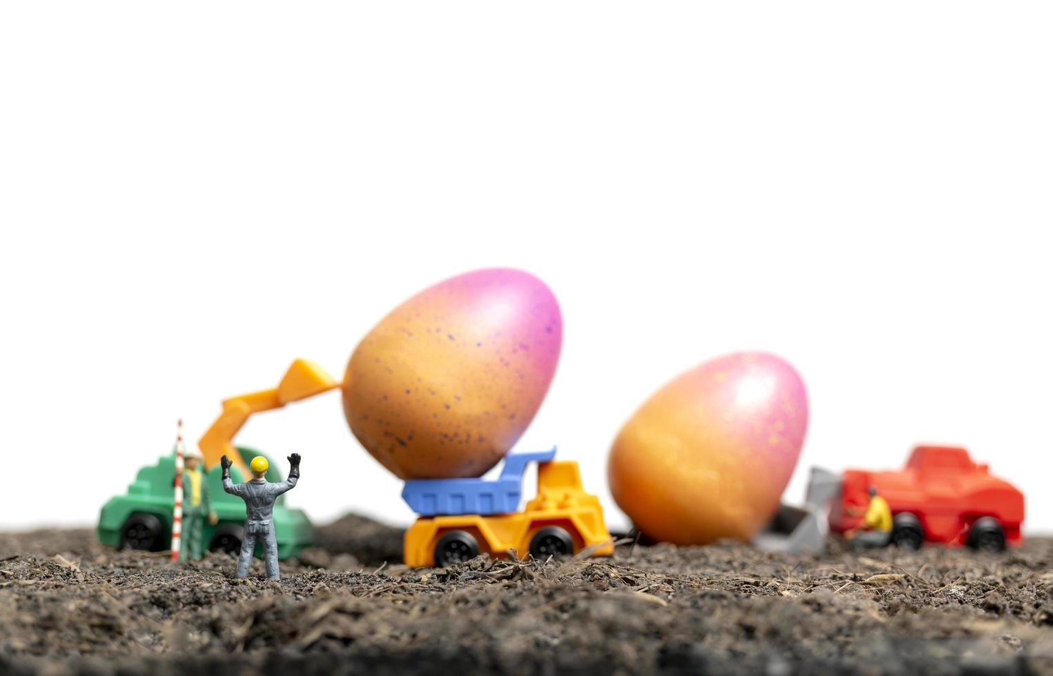 Gente en miniatura trabajando en huevos de pascua para el día de pascua con un fondo blanco. foto