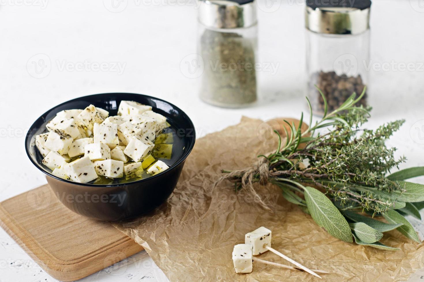 Feta marinado en un plato sobre una tabla de madera con especias sobre un fondo blanco. foto