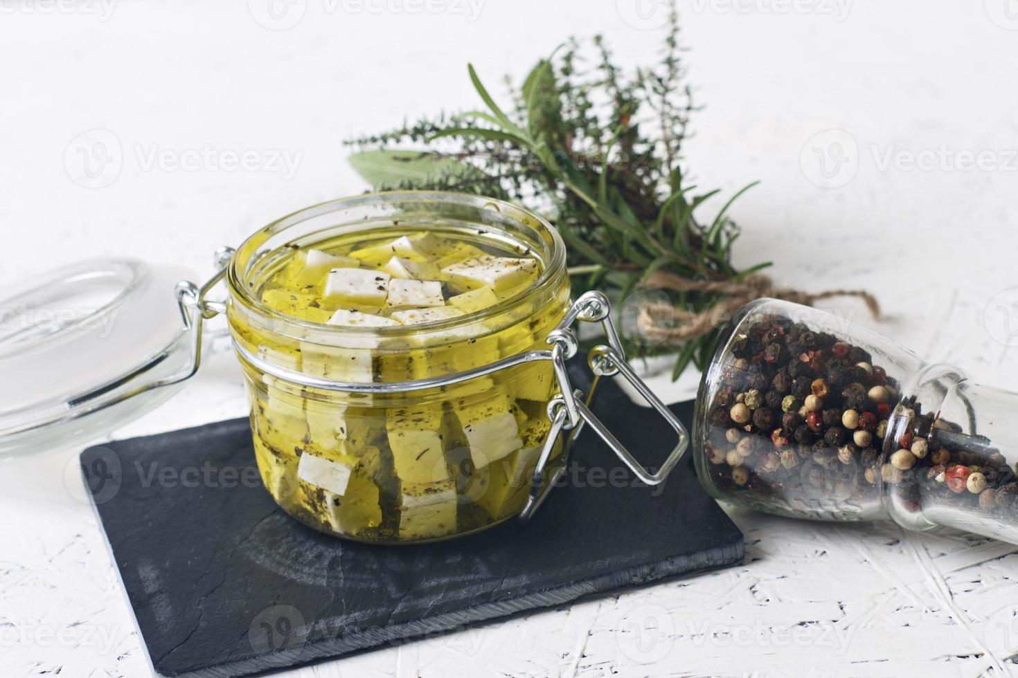 Marinated feta in a glass jar and spices against a white background photo