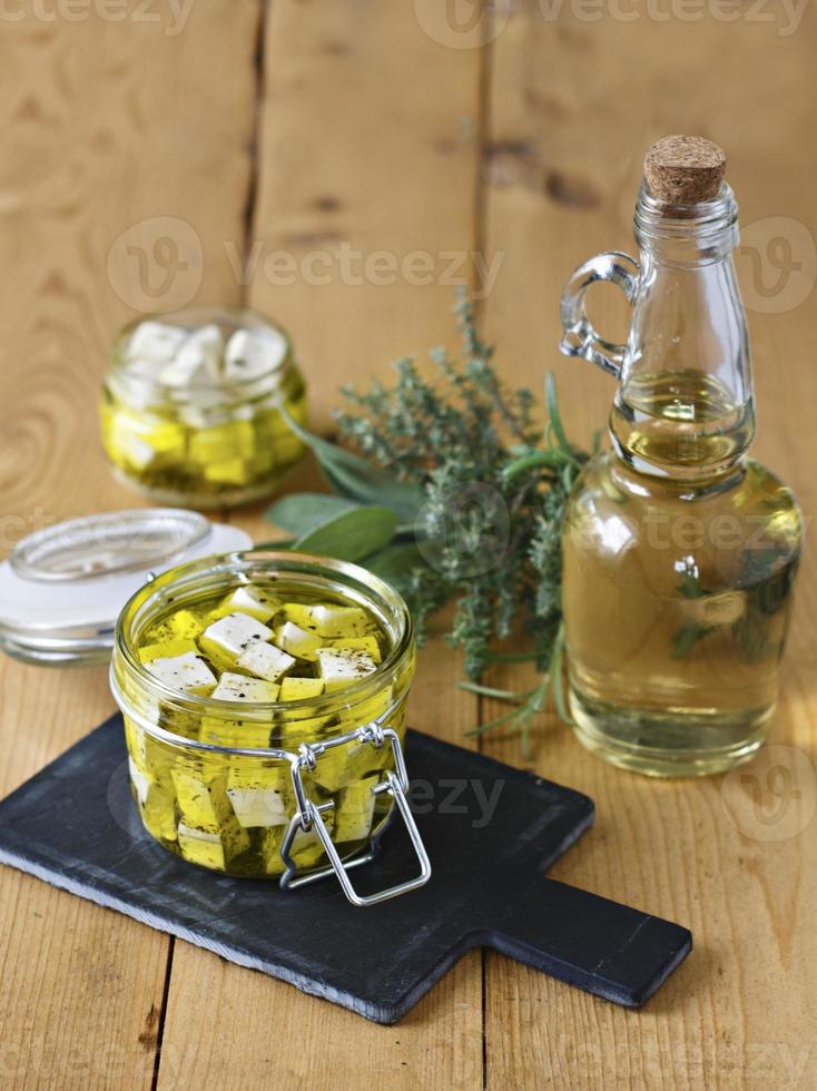 Feta marinado en un frasco de vidrio, especias y aceite de oliva sobre un fondo de madera foto