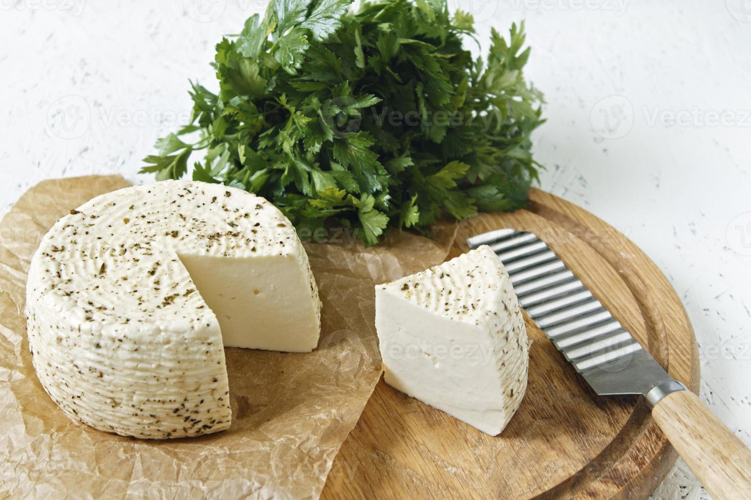 White cheese on a wooden board on a white background with greens photo