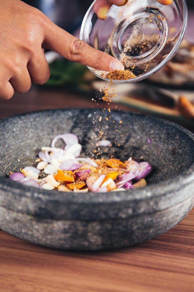 A person pouring spices in a gray bowl filled with onion rings photo