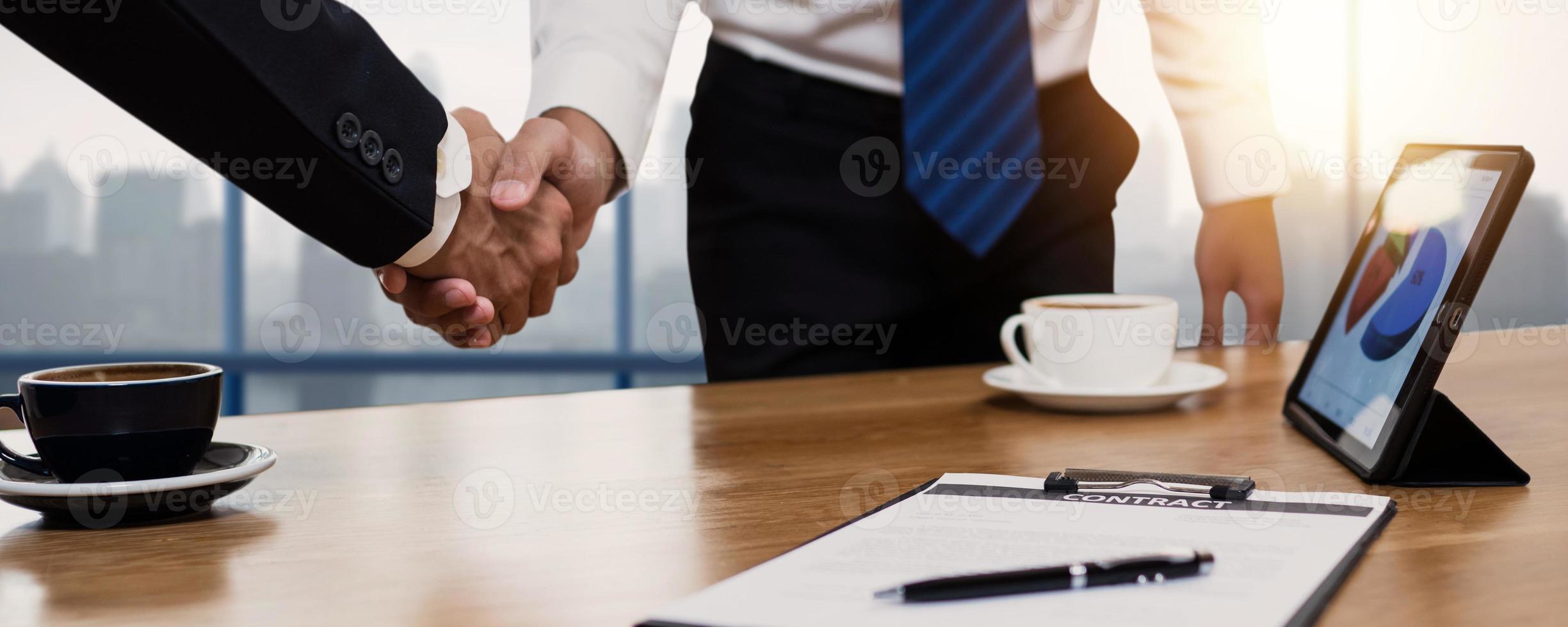 gente de negocios dándose la mano junto al escritorio con tazas de café y tableta foto