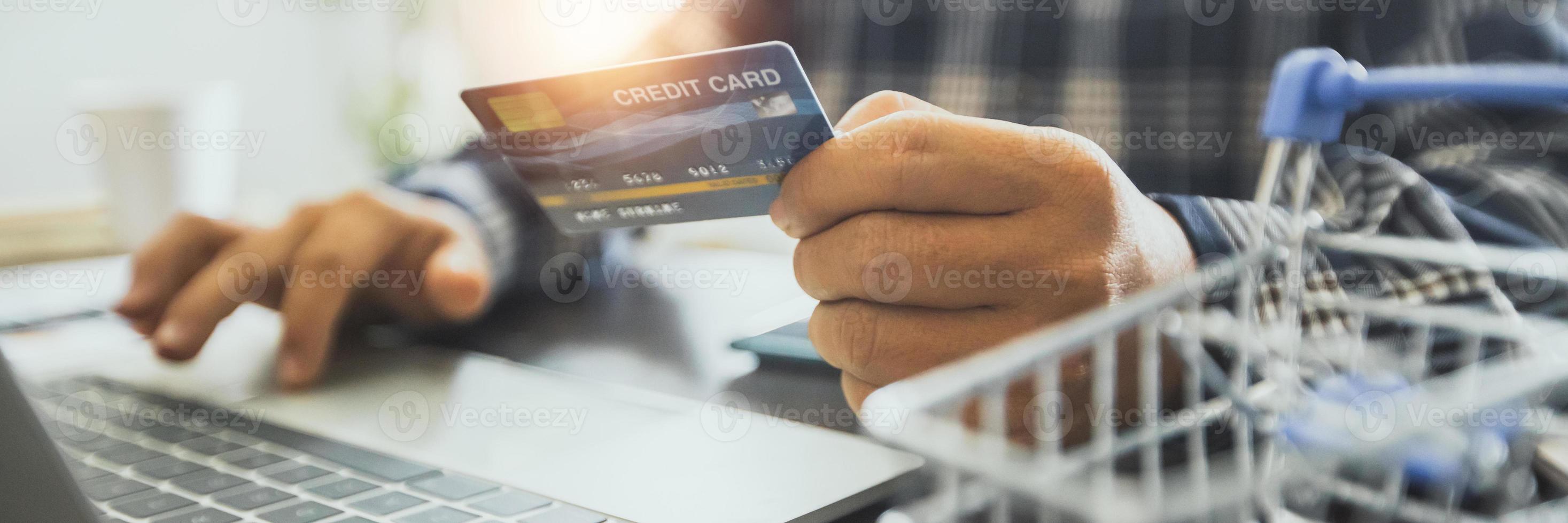 Hombre sujetando una tarjeta de crédito y trabajando en una computadora portátil foto
