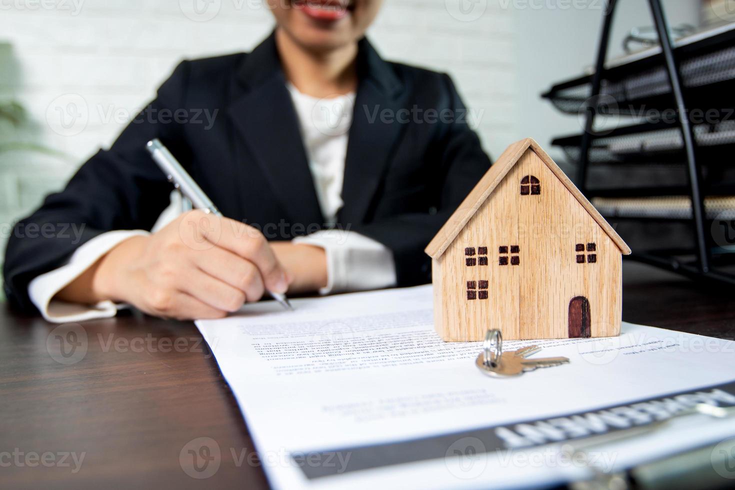 Person signing contract next to model house and keys photo