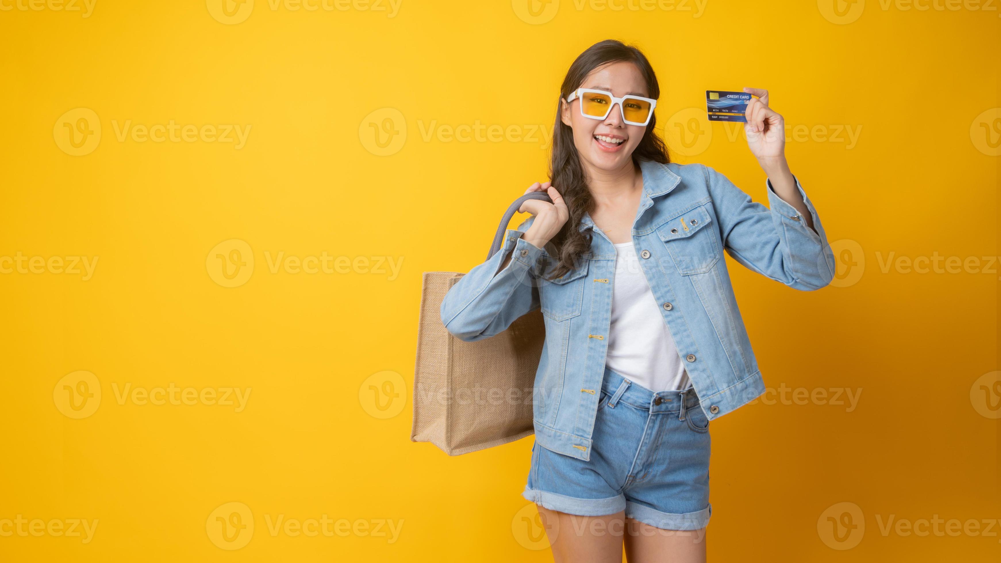 Mujer asiática sosteniendo una tarjeta de crédito y una bolsa de papel sobre fondo amarillo foto
