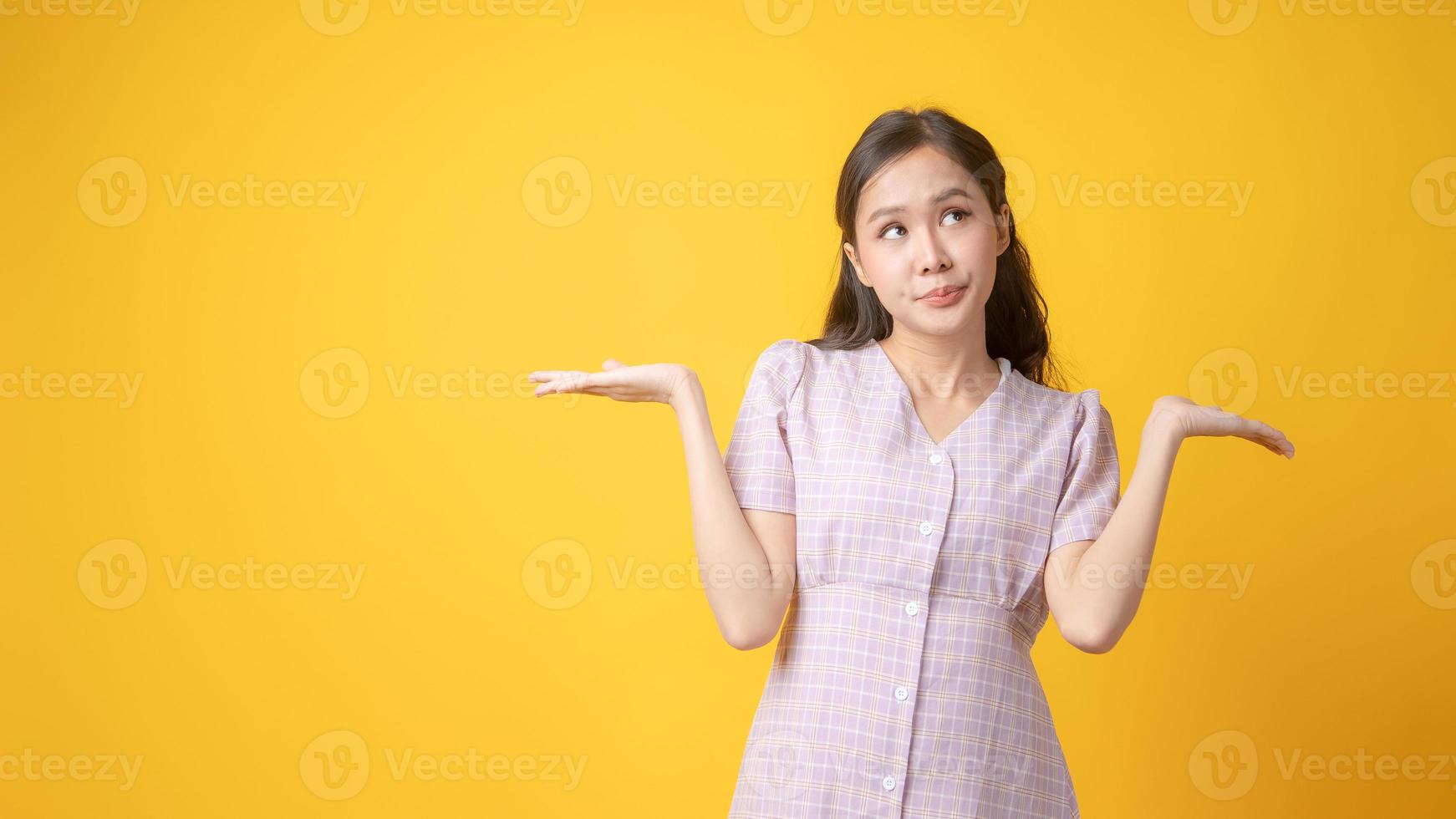 Mujer asiática gesticulando con ambas palmas hacia arriba sobre fondo amarillo foto