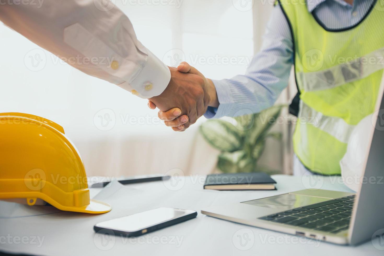 empresario y trabajador de la construcción un apretón de manos junto a la computadora portátil y el casco foto