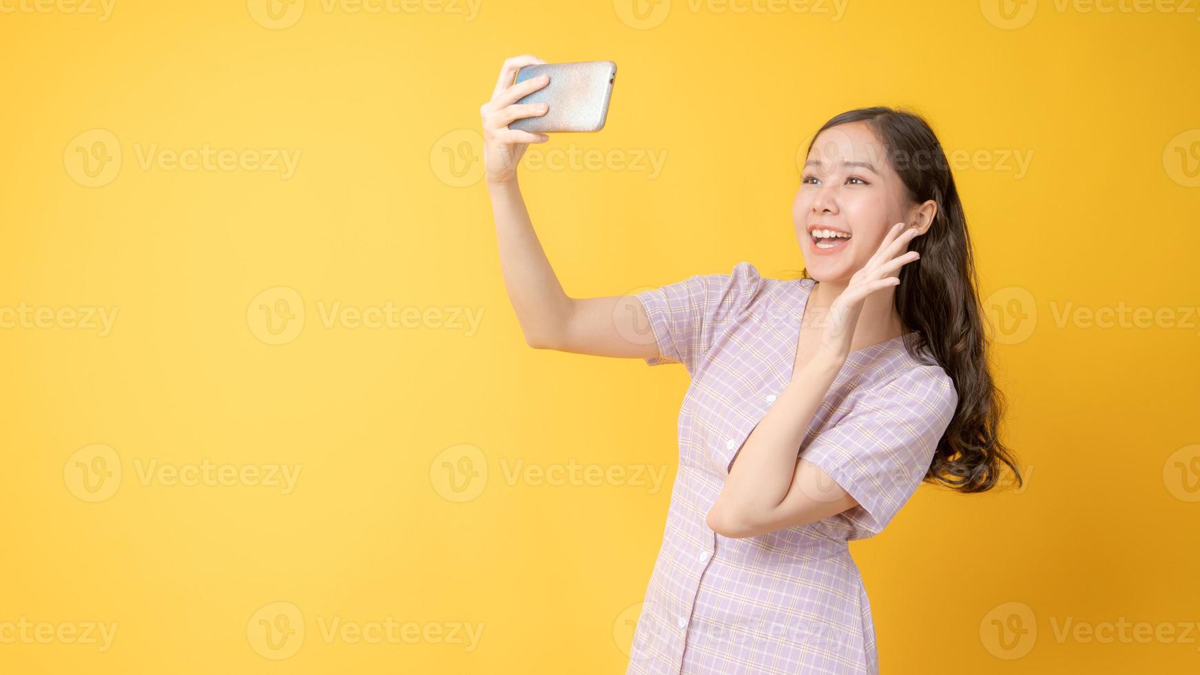 Mujer asiática sonriendo y tomando un autorretrato con un teléfono celular sobre fondo amarillo foto
