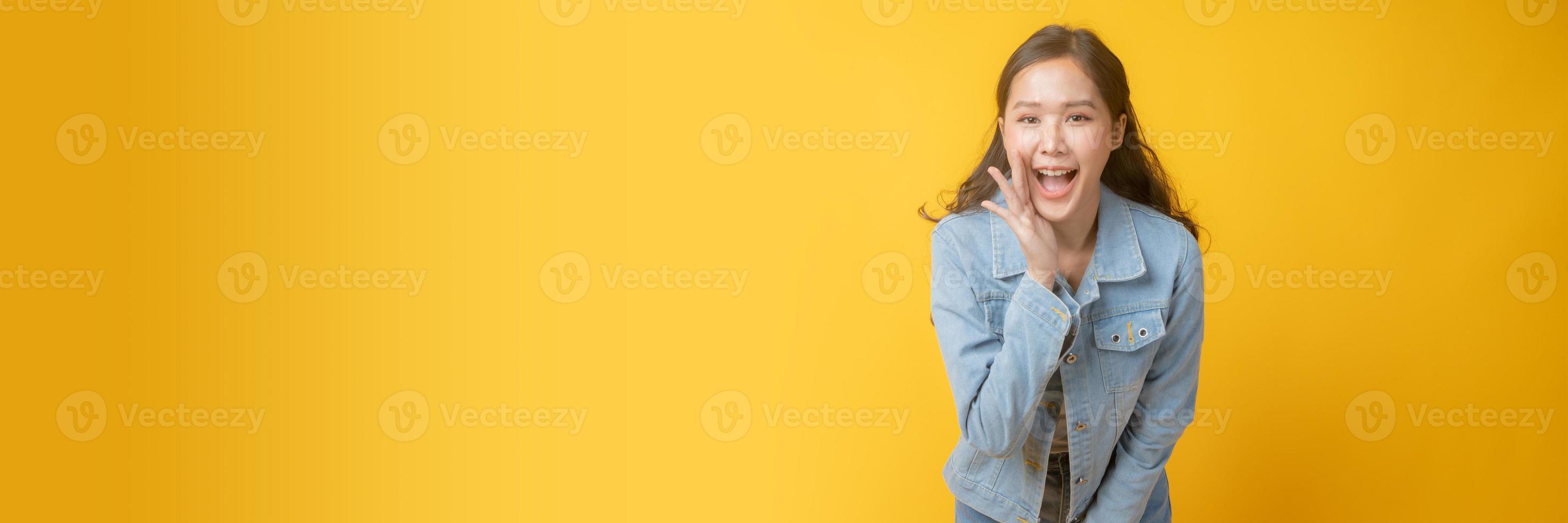 Asian woman smiling and gesturing with hand next to mouth on yellow background photo