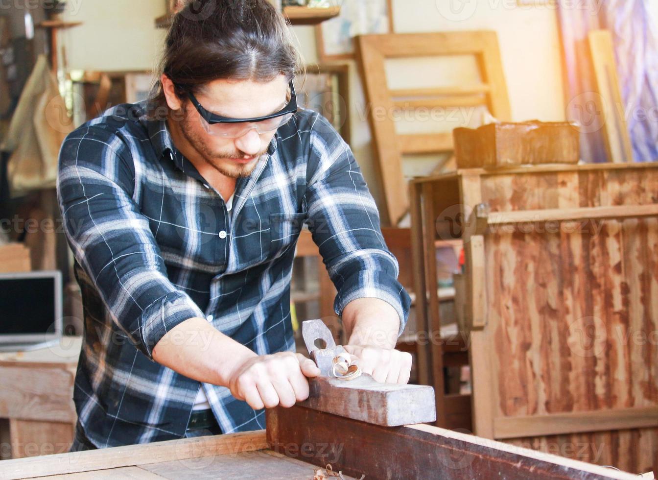 A handsome young carpenter is processing wood for furniture photo