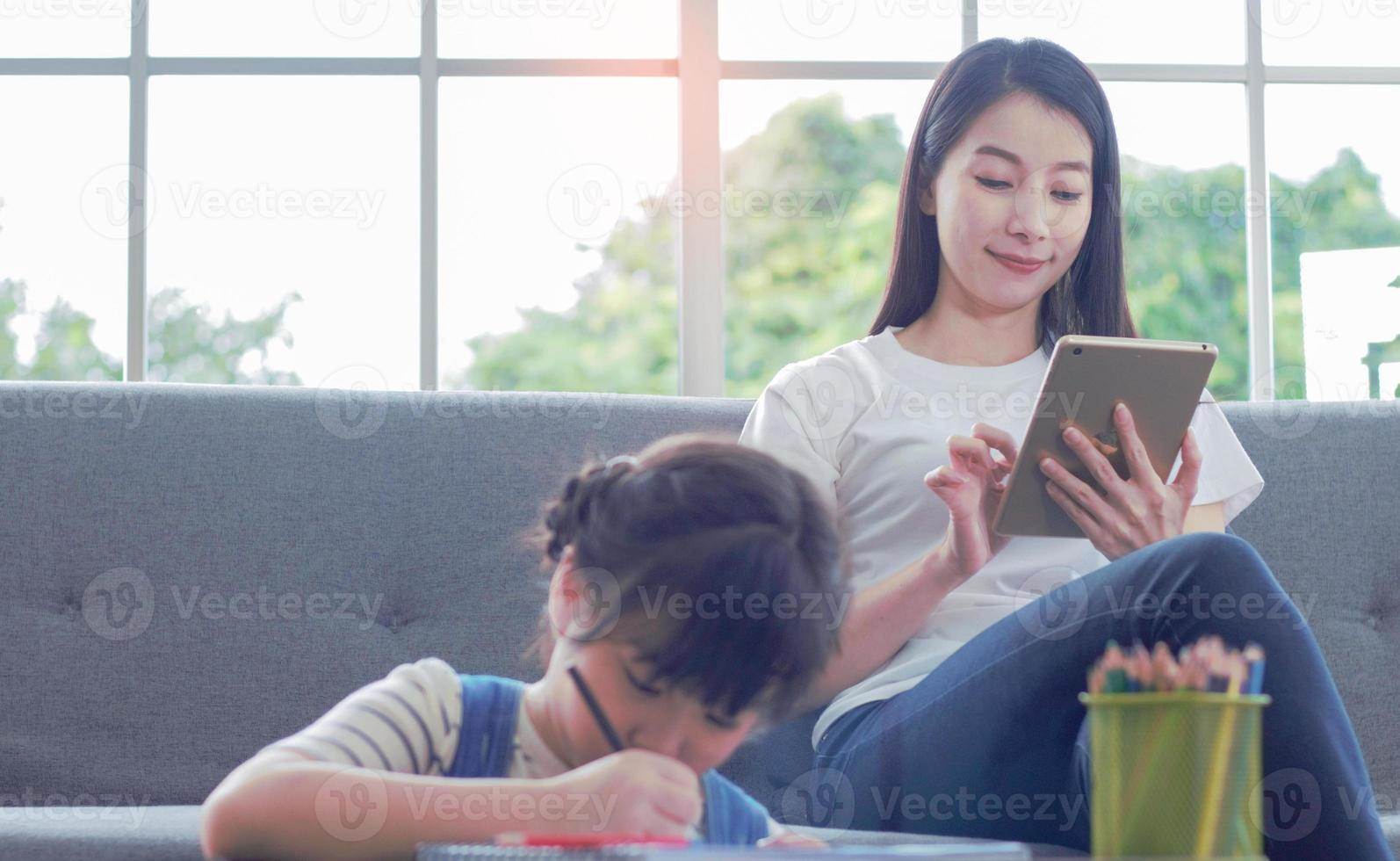 madre asiática felizmente se sienta enseñando a su hija a leer la tarea foto