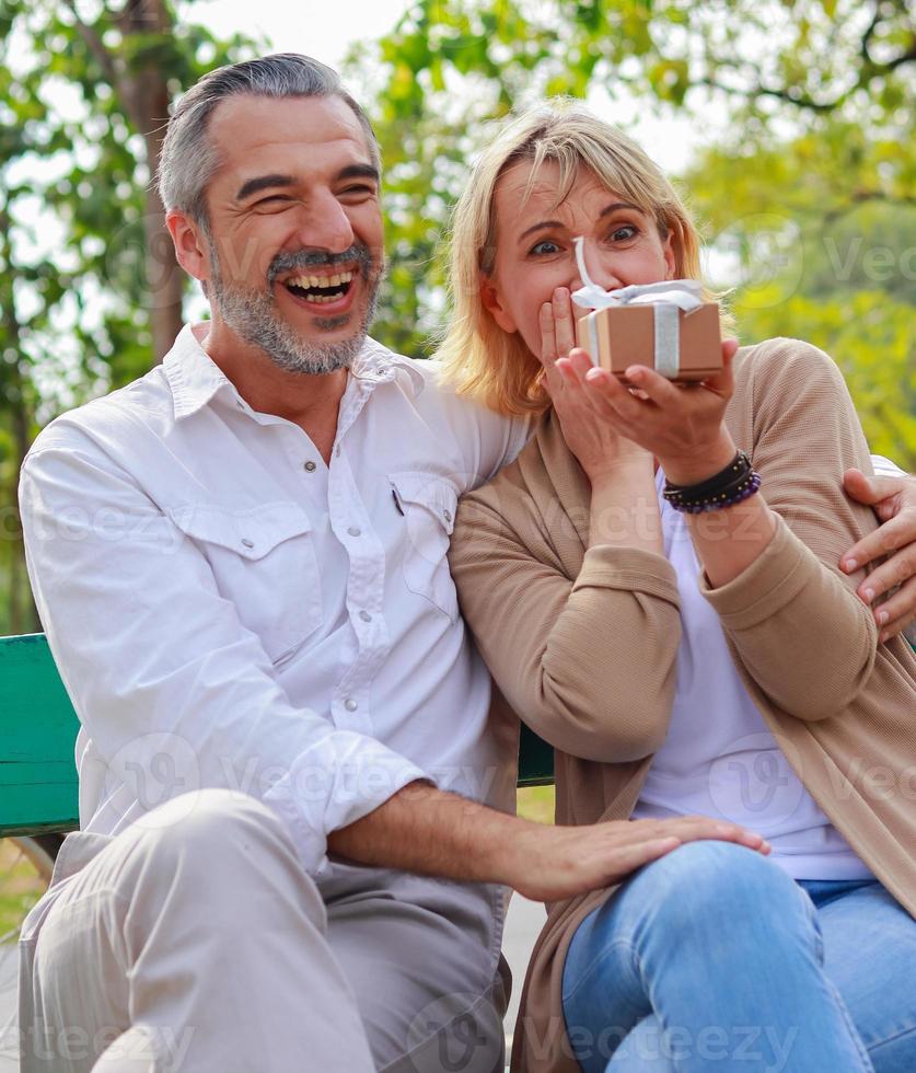 Elderly white man surprises with gift box to his beautiful girlfriend photo