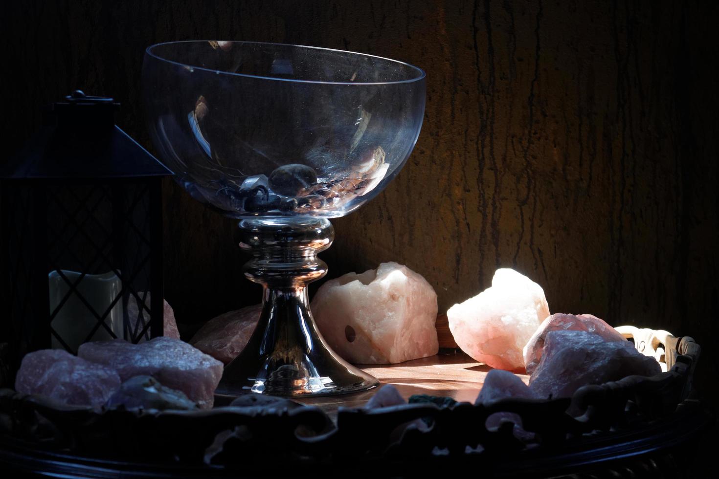 Pieces of rose quartz crystals under a spotlight next to a glass goblet photo