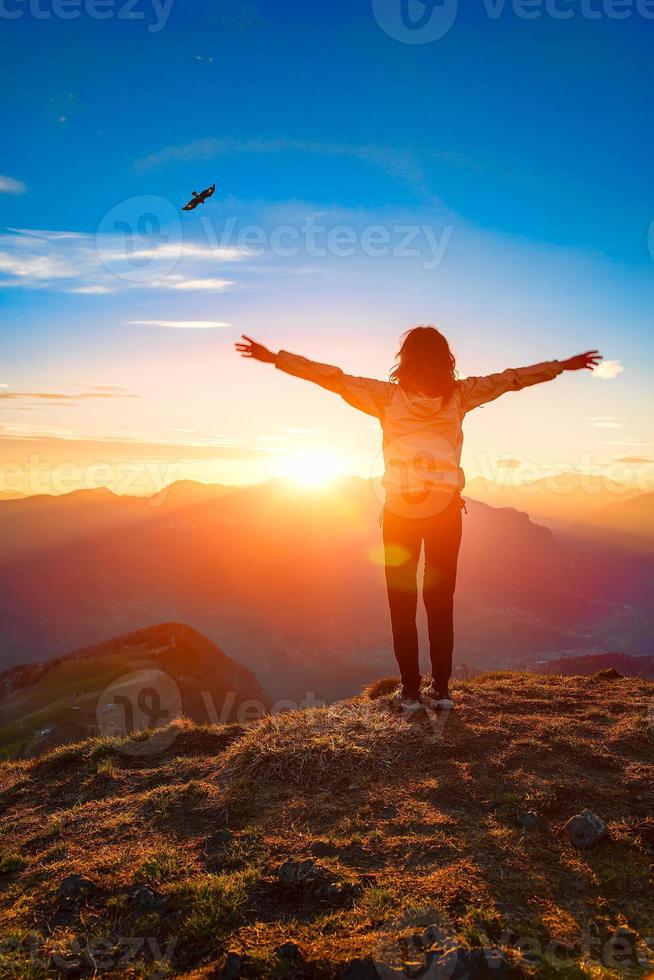 Woman on top of a mountain at sunset looks at eagle photo