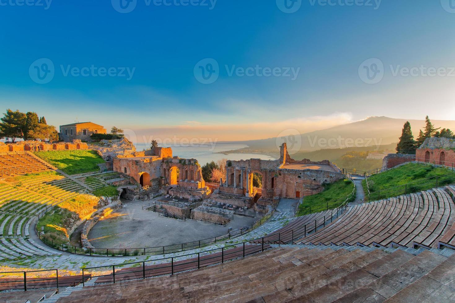 Antiguo teatro de Taormina con Etna volcán en erupción al atardecer foto