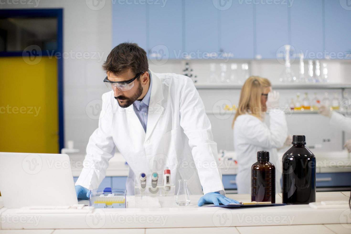 Researcher in white lab coat working using laptop while sitting in the lab photo