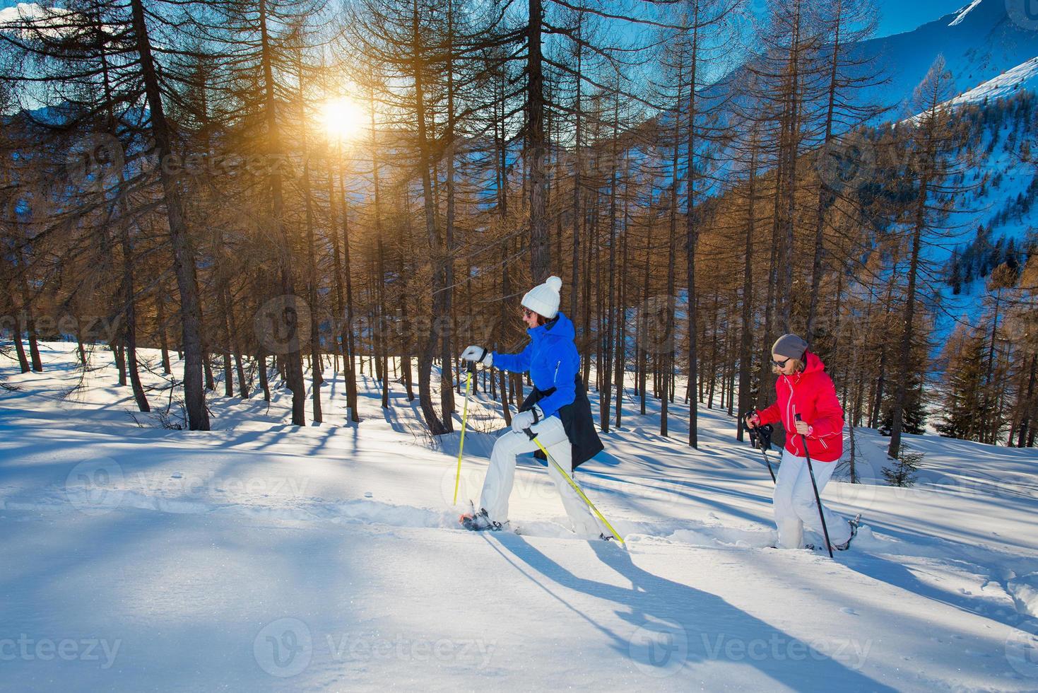 Couple of girlfriends walk with snowshoes at sunset, stock photo