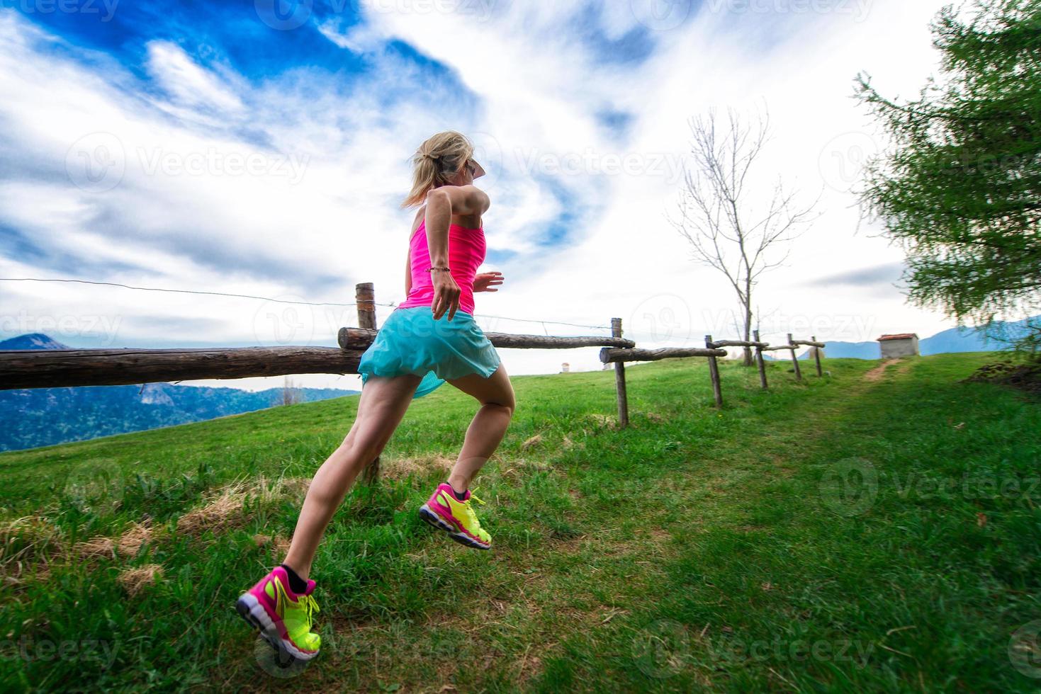Atleta chica rubia corre un sendero de montaña en la hierba verde foto