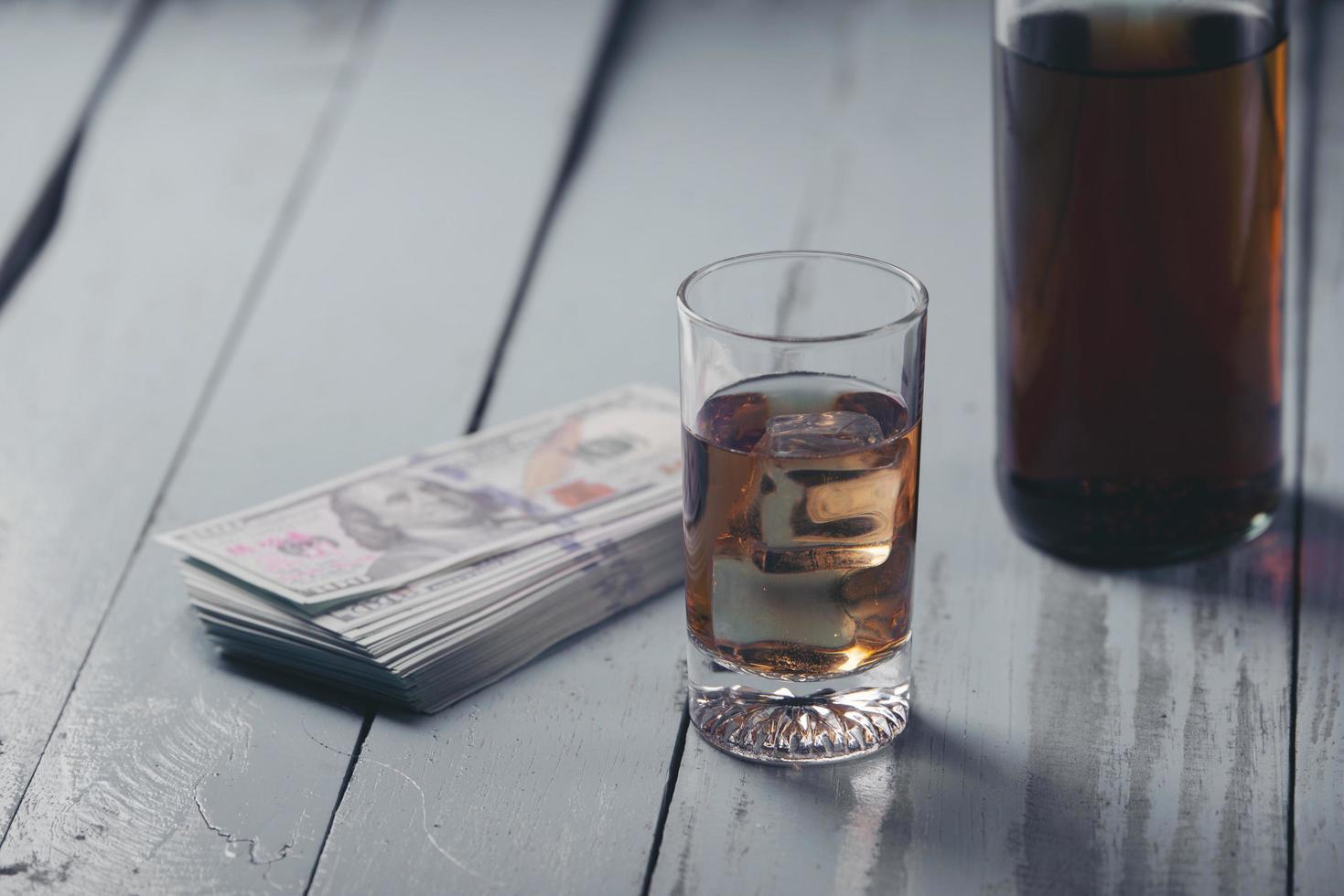 Bodegón con vaso y botella de alcohol y dinero en efectivo en la mesa de madera foto