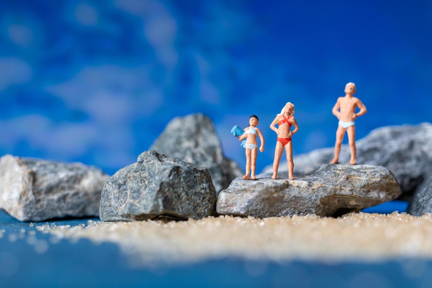 Miniature people wearing swimsuits relaxing on the beach with a blue background, summertime concept photo