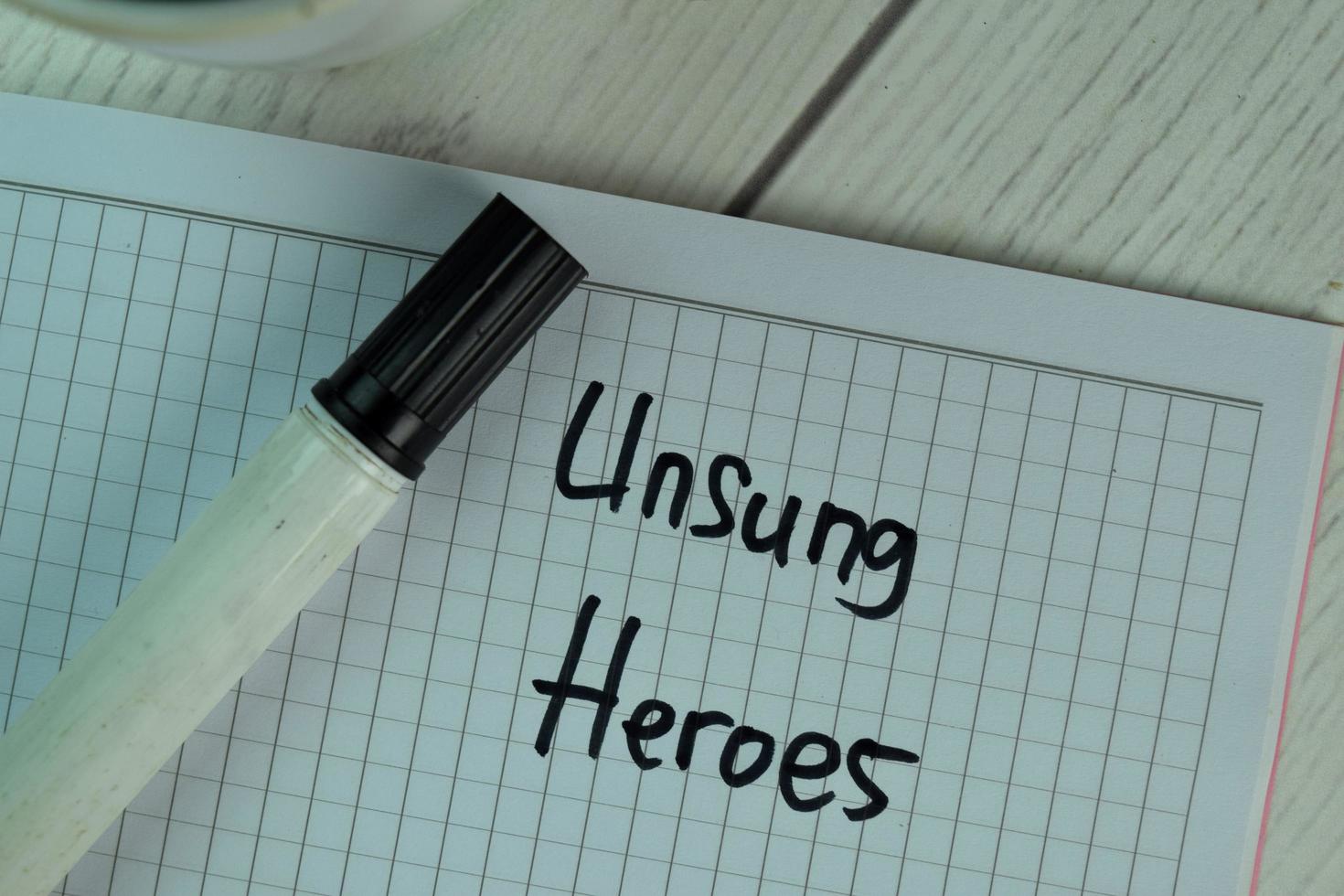 Unsung Heroes written on sticky note isolated on wooden table photo