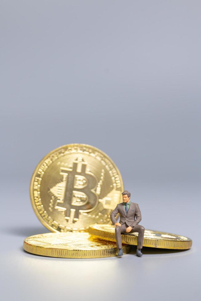 Empresario en miniatura sentado en monedas bitcoin, concepto de inversión futura foto