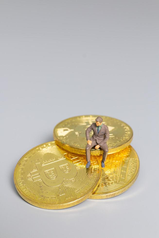 Empresario en miniatura sentado en monedas bitcoin, concepto de inversión futura foto
