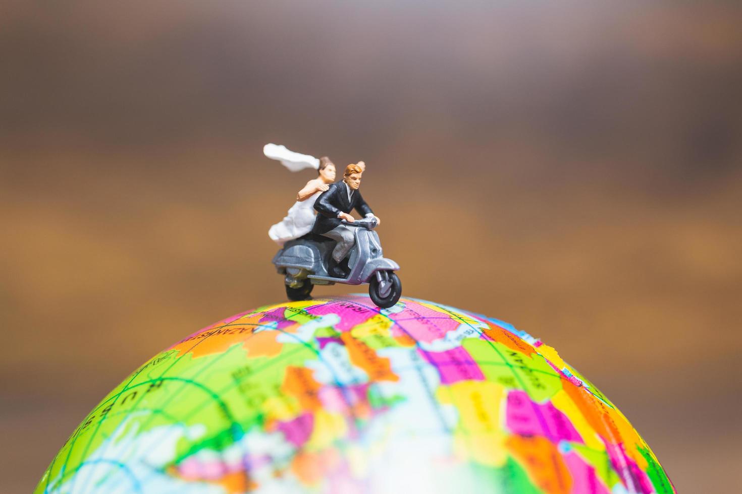 Miniature couple riding a motorcycle on a world globe photo