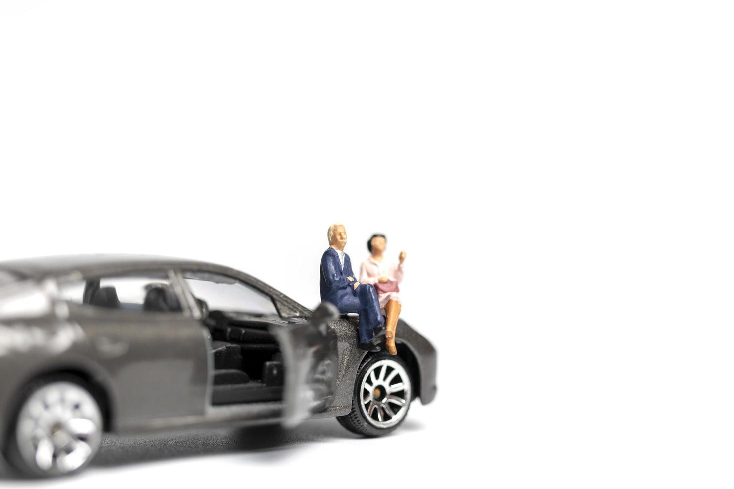 Miniature people sitting on a car on a white background photo