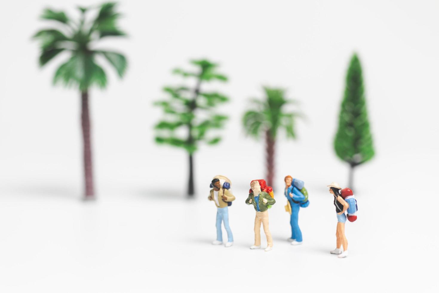 Viajeros en miniatura con mochilas caminando sobre un fondo blanco, concepto de viaje y aventura foto