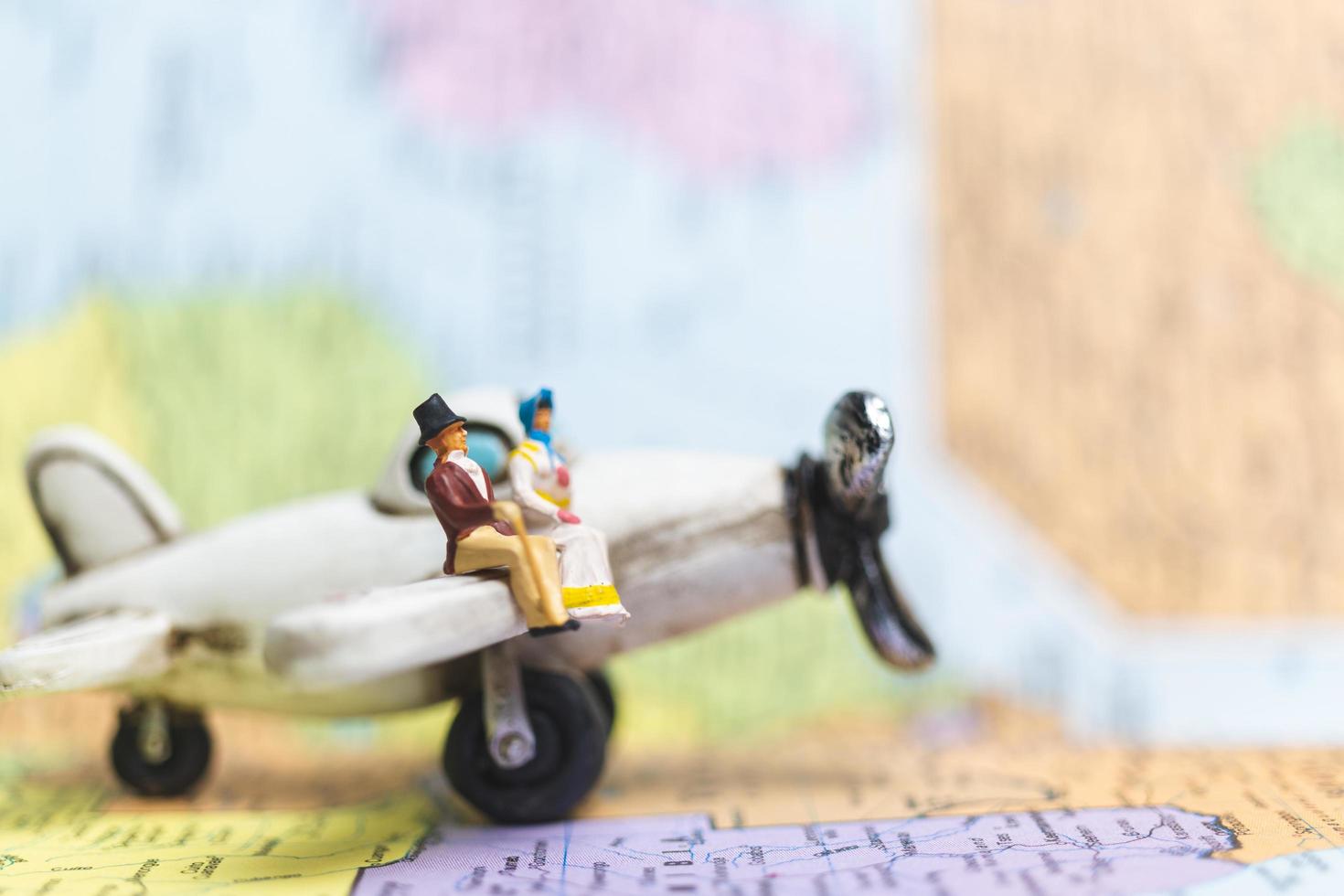 Gente en miniatura sentada en un avión con un fondo de mapa del mundo, concepto de viaje foto