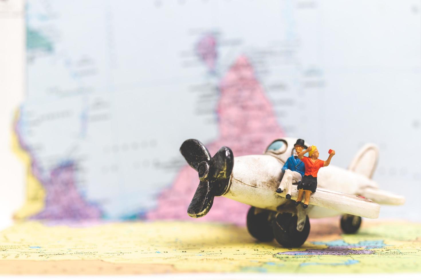 Miniature people sitting on an airplane with a world map background, travel concept photo