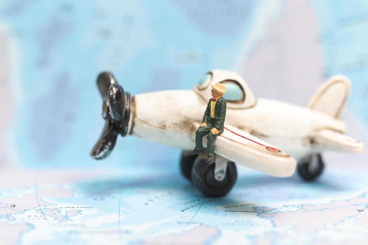 Miniature person sitting on an airplane with a world map background, travel concept photo