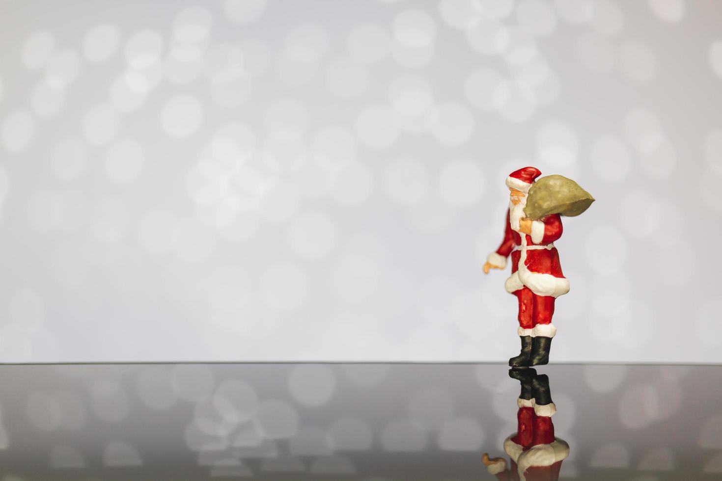 Miniature Santa Claus carrying a bag on a bokeh background, Merry Christmas and Happy New Year concept. photo