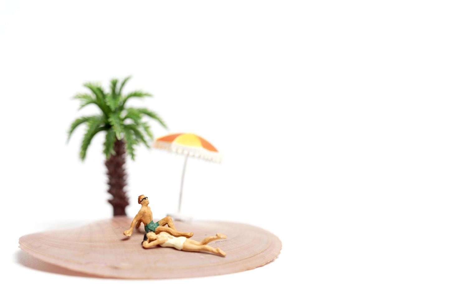 Miniature people wearing swimsuits relaxing on a seashell on a white background photo