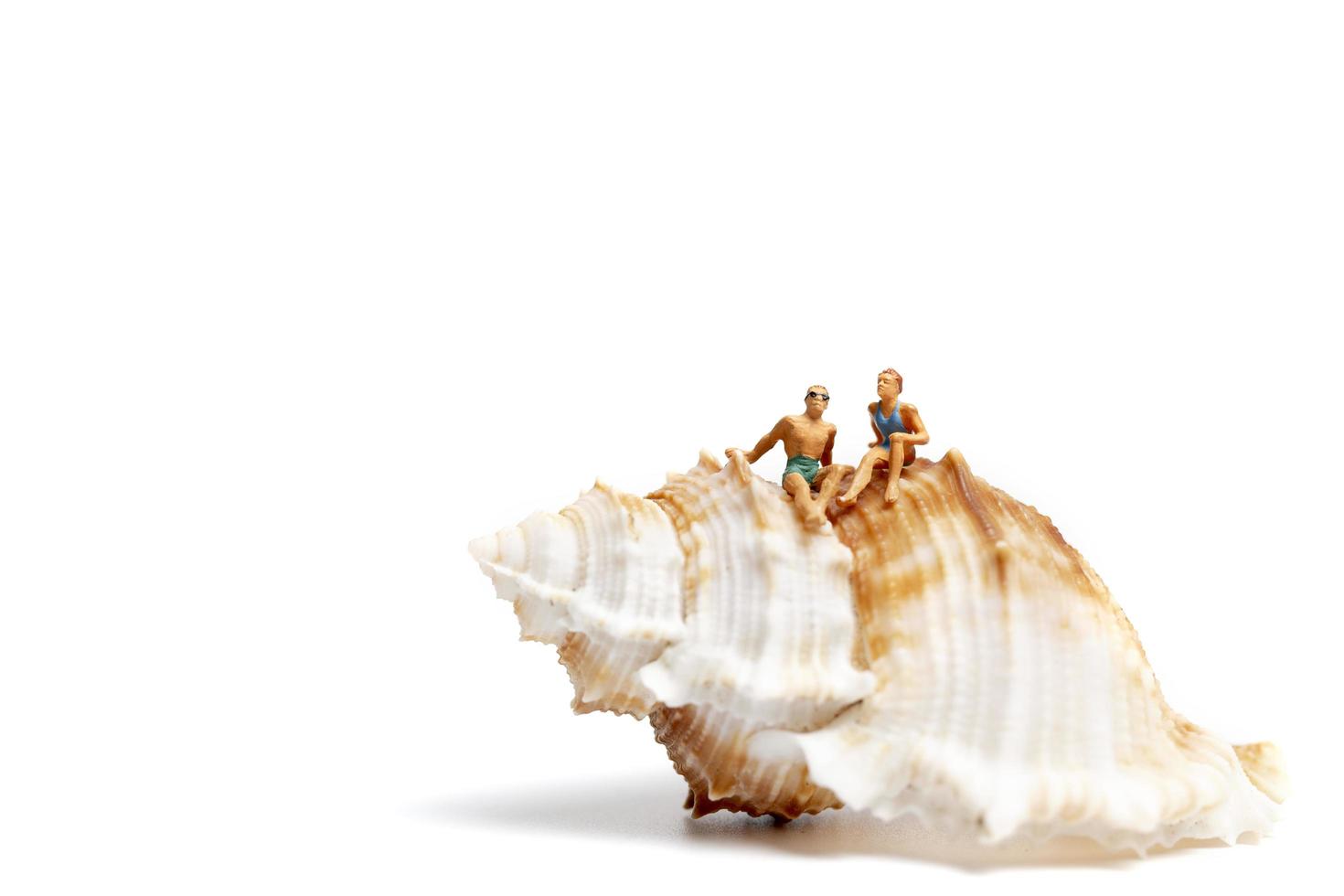 Miniature people wearing swimsuits relaxing on a seashell on a white background photo