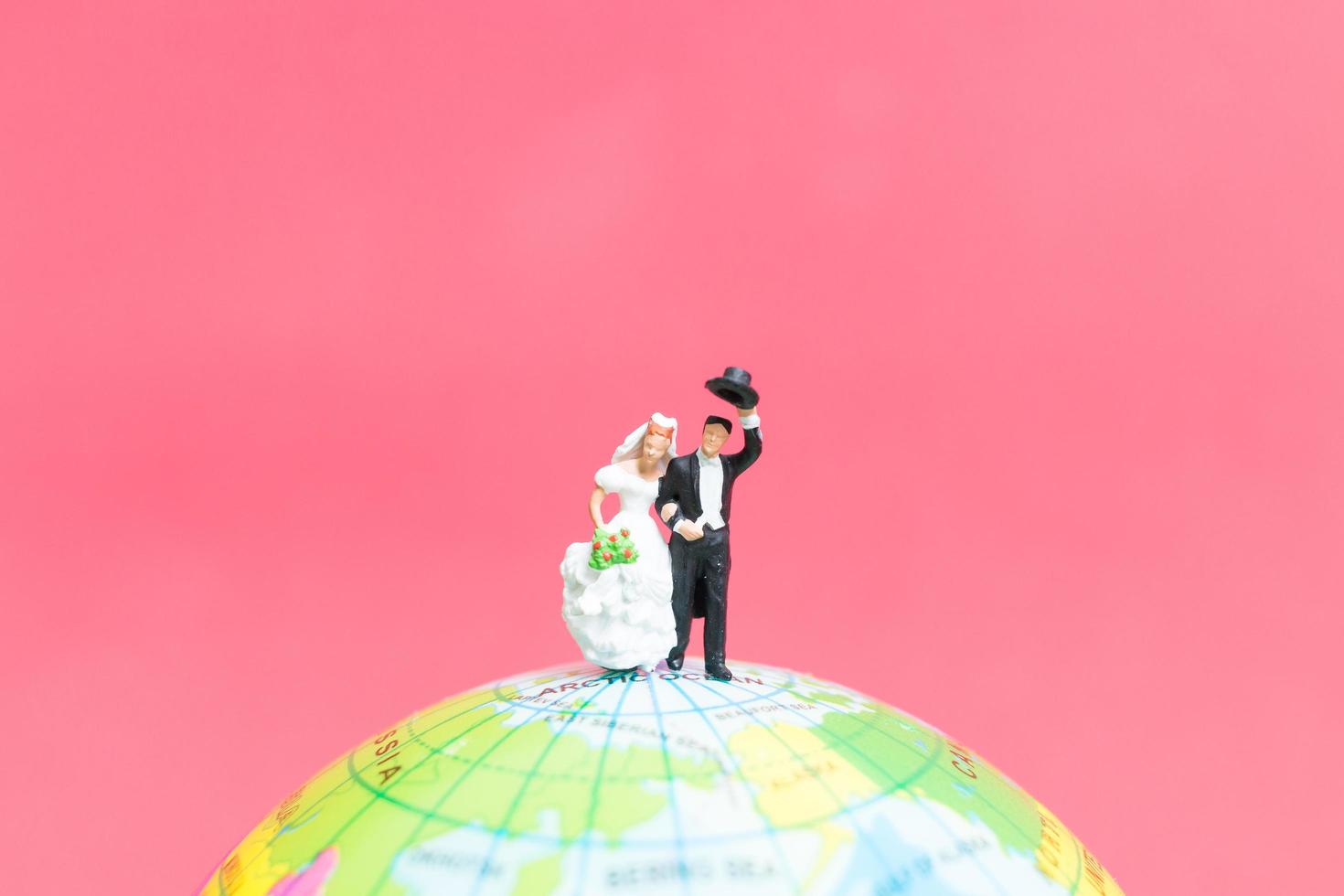 Miniature bride and groom on a globe with a pink background, Valentine's Day concept photo