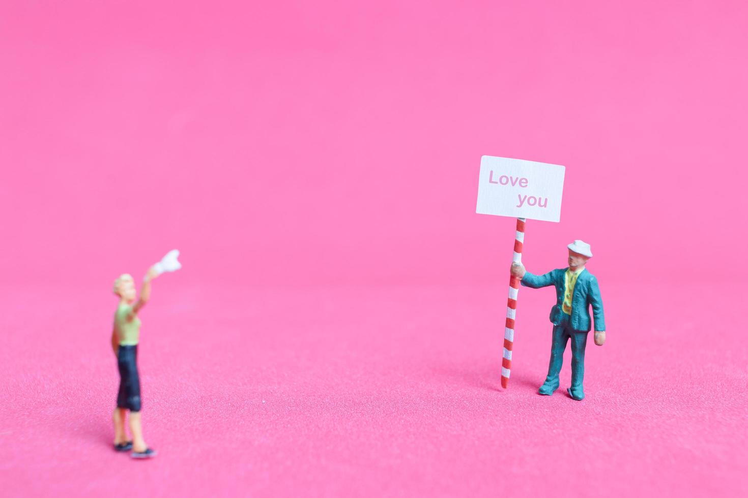 Persona en miniatura sosteniendo un tablero de papel con te amo sobre un fondo rosa, concepto del día de San Valentín foto