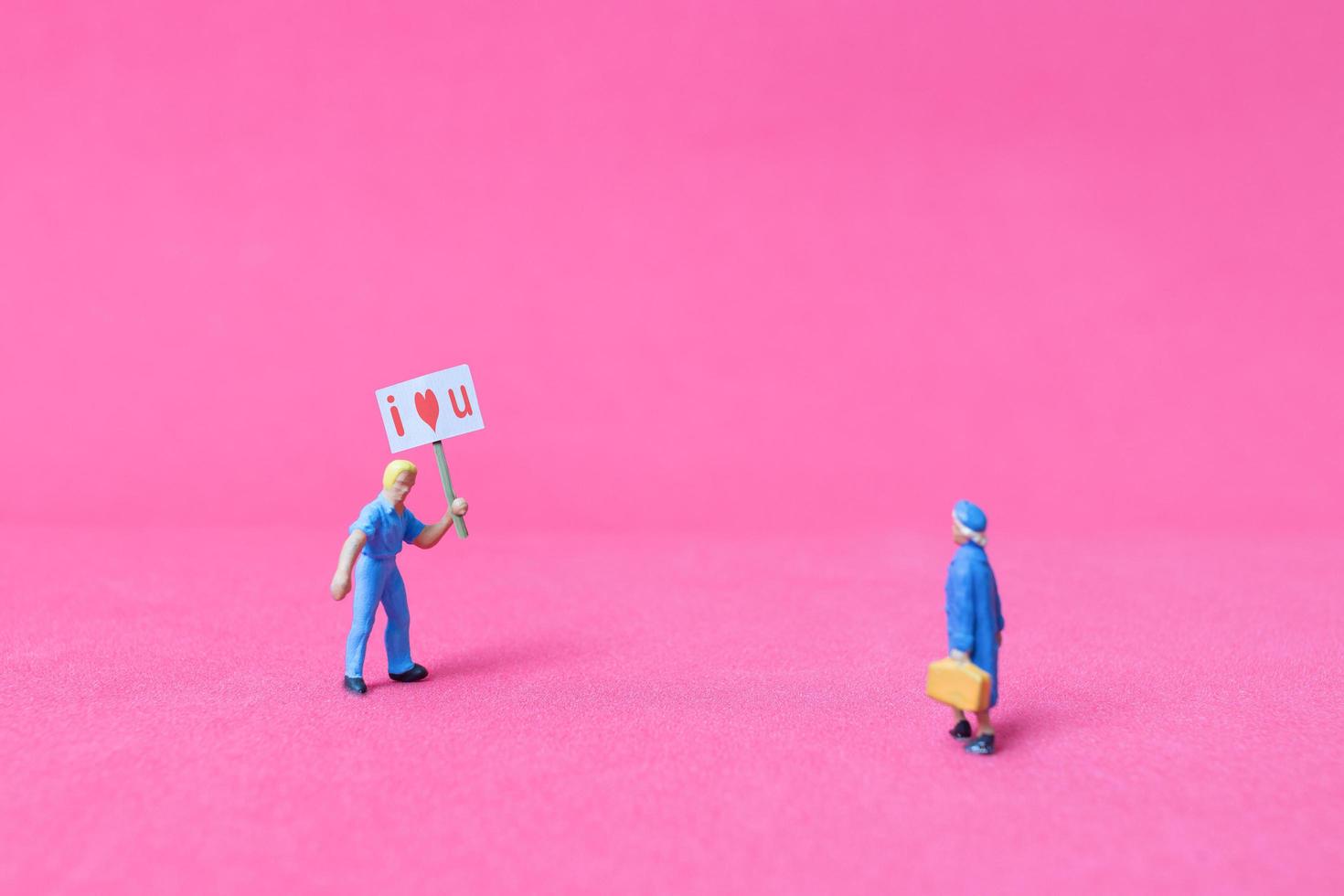 Miniature person holding a paper board with I love you on a pink background, Valentine's Day concept photo