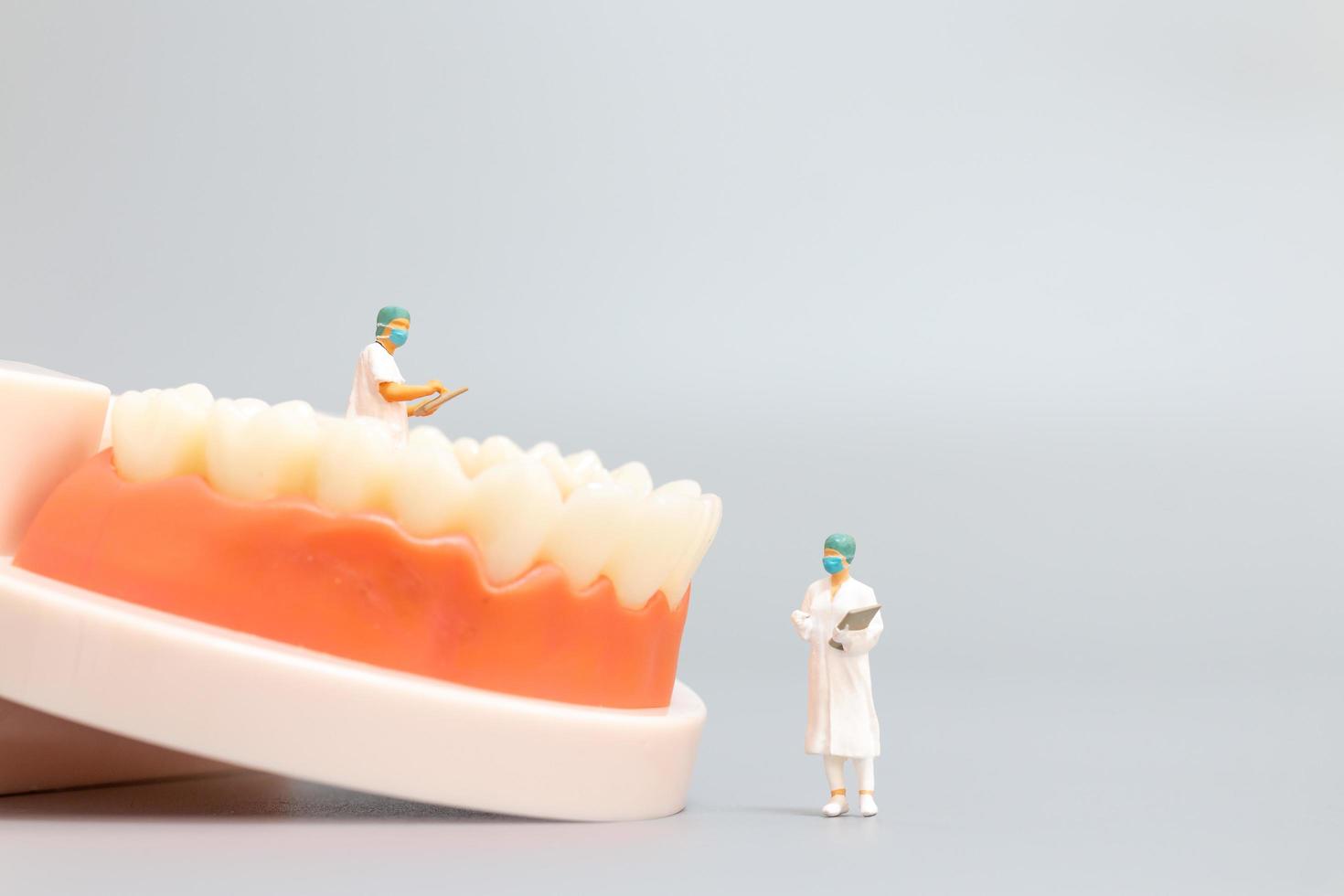 Dentista en miniatura que repara dientes humanos con encías y esmalte, concepto médico y de salud foto